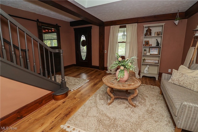 foyer entrance with wood-type flooring, a textured ceiling, a barn door, and beamed ceiling