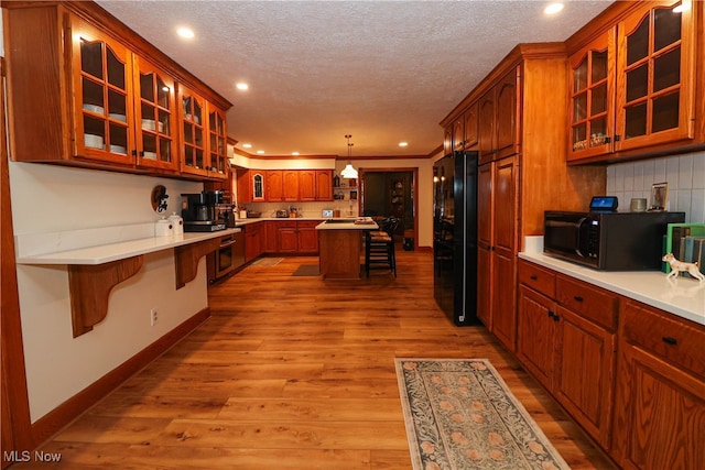 kitchen with hanging light fixtures, a breakfast bar, black appliances, a textured ceiling, and light hardwood / wood-style floors