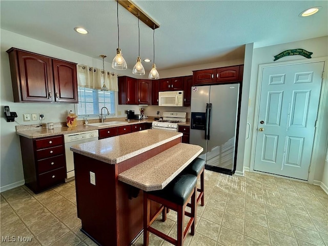 kitchen with white appliances, sink, a kitchen island, hanging light fixtures, and a breakfast bar area