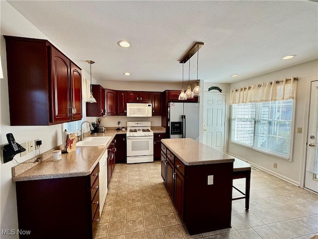 kitchen featuring pendant lighting, white appliances, sink, a textured ceiling, and a kitchen island