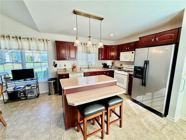 kitchen featuring a kitchen bar, white appliances, sink, a center island, and hanging light fixtures