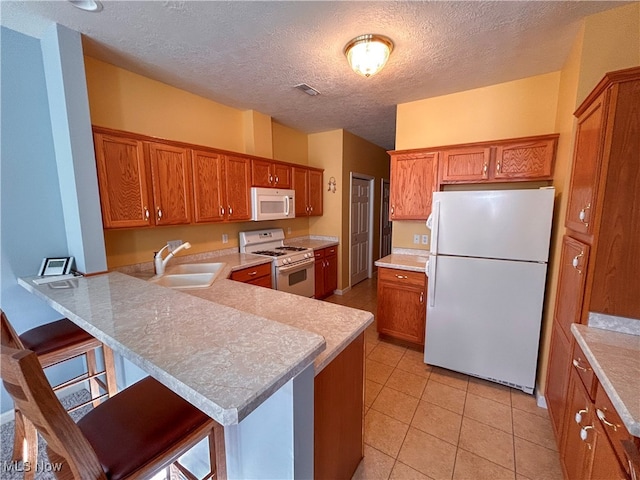 kitchen featuring white appliances, sink, a textured ceiling, kitchen peninsula, and a breakfast bar area