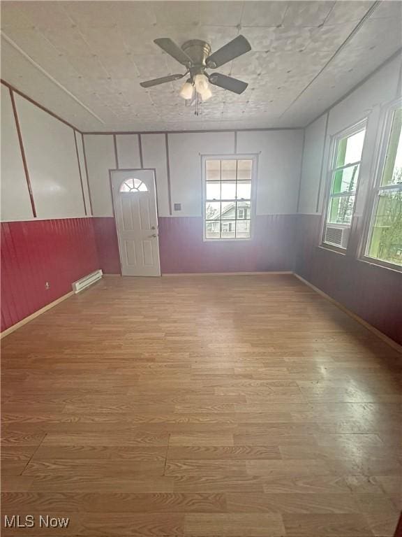 unfurnished room with baseboard heating, ceiling fan, a healthy amount of sunlight, and light wood-type flooring