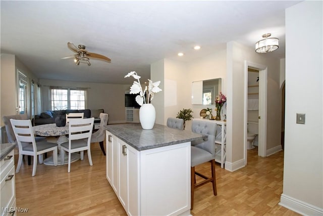 kitchen featuring white cabinetry, a kitchen bar, ceiling fan, light hardwood / wood-style floors, and dark stone counters