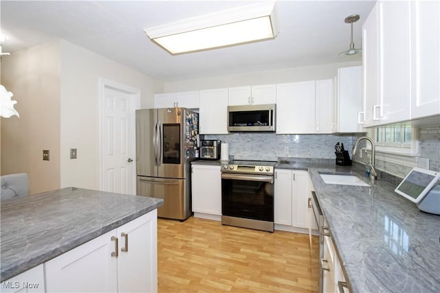 kitchen with decorative light fixtures, stainless steel appliances, backsplash, white cabinets, and sink