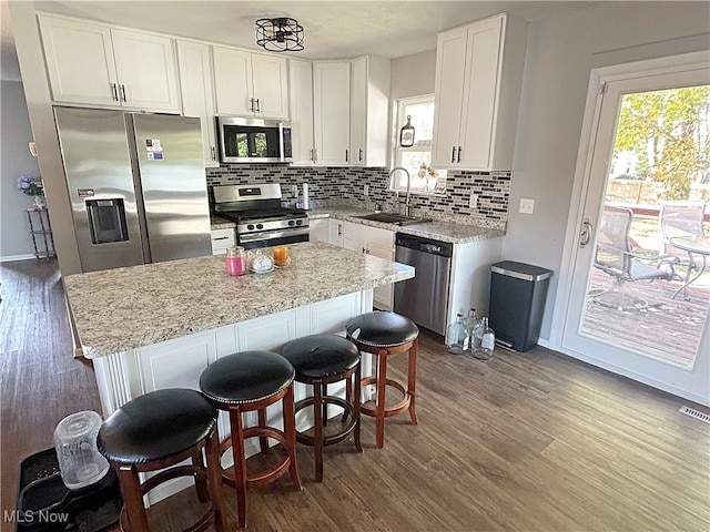 kitchen featuring decorative backsplash, hardwood / wood-style floors, a center island, white cabinets, and appliances with stainless steel finishes