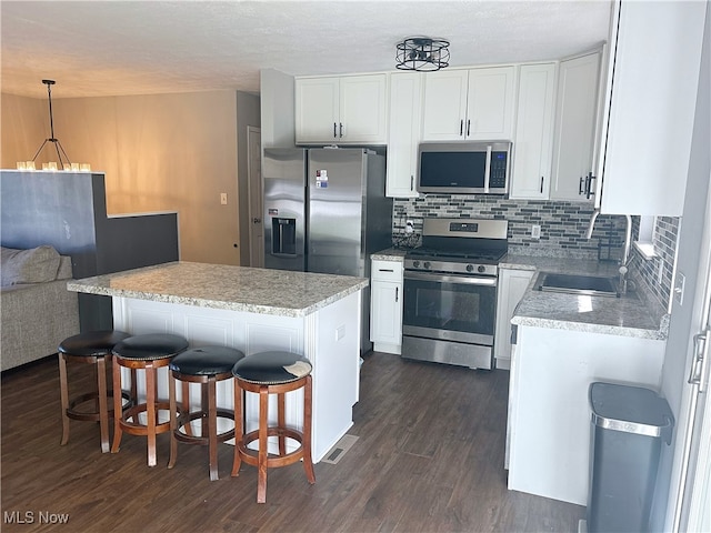 kitchen with dark wood-type flooring, appliances with stainless steel finishes, hanging light fixtures, and white cabinetry