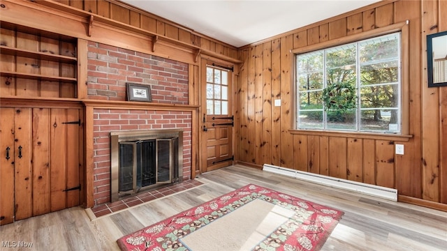 living room featuring light hardwood / wood-style flooring, a baseboard heating unit, a brick fireplace, and wooden walls