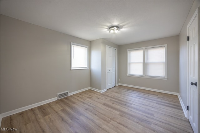 unfurnished bedroom with light hardwood / wood-style flooring, multiple windows, a textured ceiling, and a closet