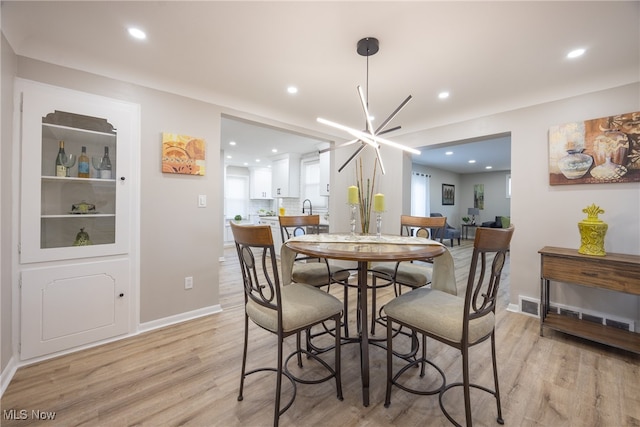 dining space with sink, an inviting chandelier, and light wood-type flooring