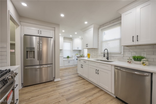 kitchen with light hardwood / wood-style flooring, backsplash, sink, white cabinetry, and appliances with stainless steel finishes