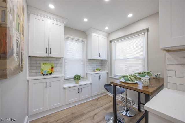 kitchen with decorative backsplash, white cabinets, a healthy amount of sunlight, and light hardwood / wood-style floors