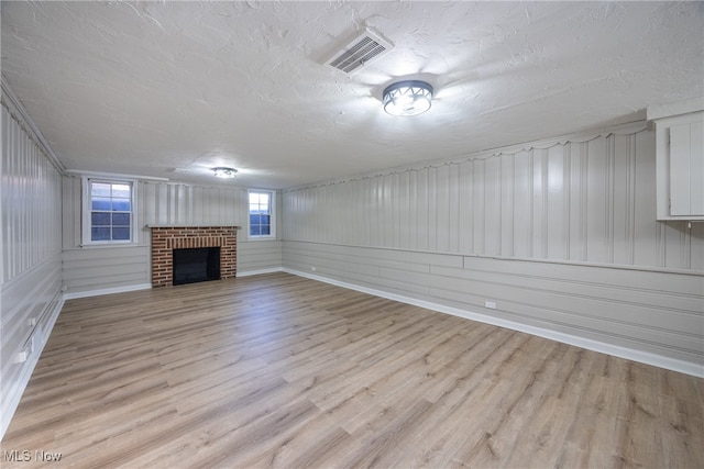 unfurnished living room with wooden walls, a brick fireplace, a textured ceiling, and light hardwood / wood-style floors