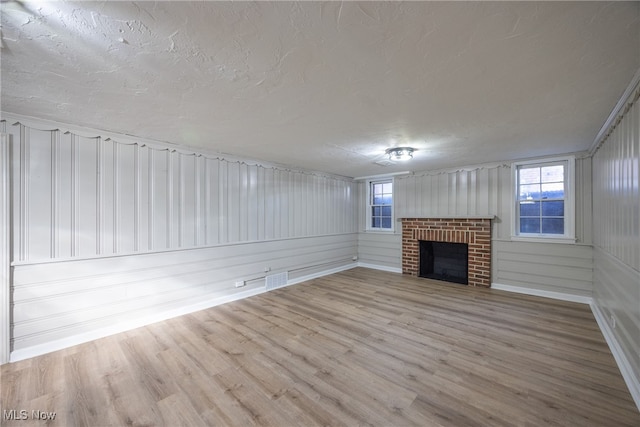 unfurnished living room with plenty of natural light, a textured ceiling, a brick fireplace, and light wood-type flooring