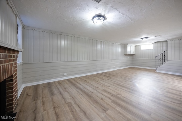 basement with light hardwood / wood-style floors, a textured ceiling, wooden walls, and a fireplace