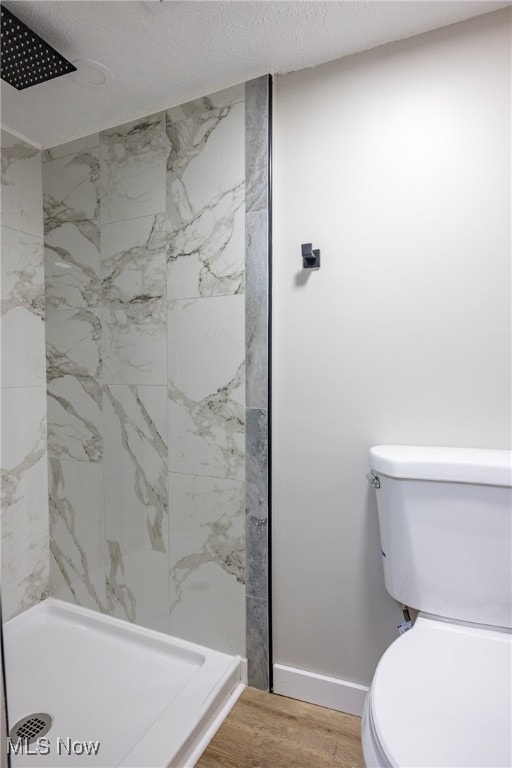 bathroom featuring a tile shower, toilet, hardwood / wood-style flooring, and a textured ceiling