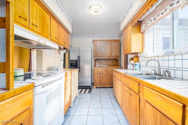 kitchen with stainless steel fridge, white electric range oven, light tile patterned flooring, tile counters, and sink