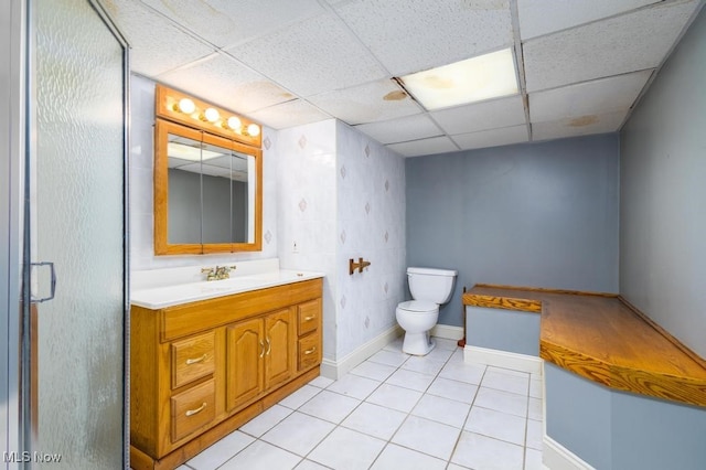 bathroom with toilet, a paneled ceiling, tile patterned floors, walk in shower, and vanity