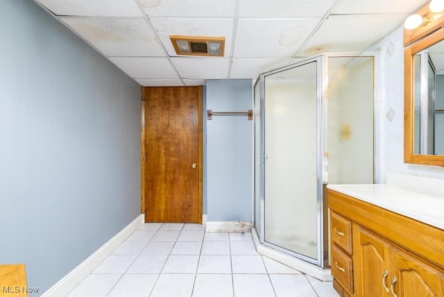 bathroom with a shower with door, vanity, a drop ceiling, and tile patterned flooring