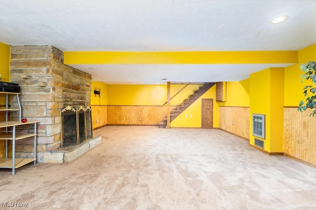 unfurnished living room with light carpet, a textured ceiling, a stone fireplace, and wooden walls