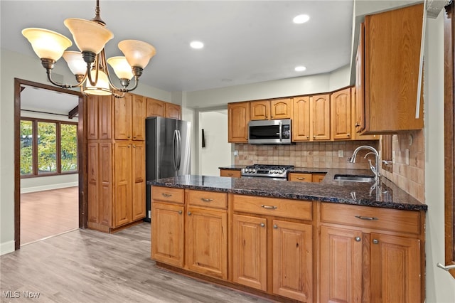 kitchen with a chandelier, light wood-type flooring, stainless steel appliances, sink, and decorative light fixtures