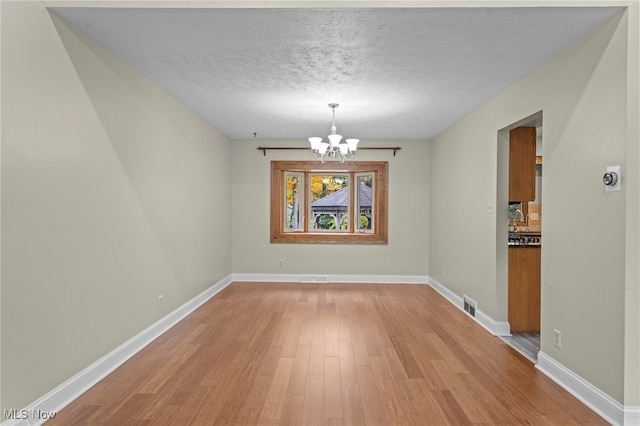 unfurnished dining area with light hardwood / wood-style flooring, a notable chandelier, and a textured ceiling