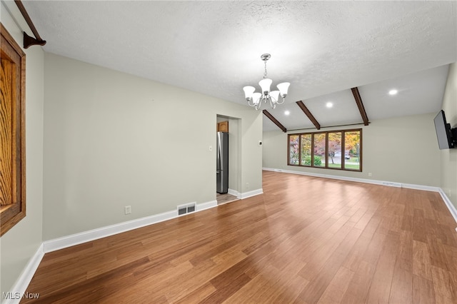 unfurnished living room featuring a notable chandelier, a textured ceiling, vaulted ceiling with beams, and hardwood / wood-style flooring