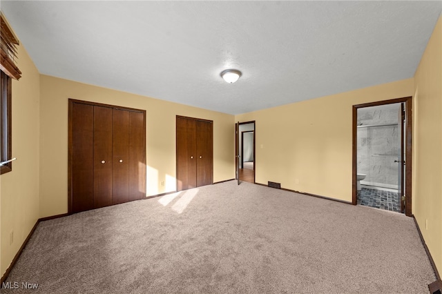 unfurnished bedroom with carpet floors, two closets, and connected bathroom