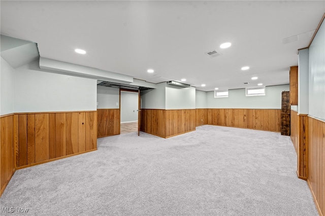 basement featuring light carpet and wood walls