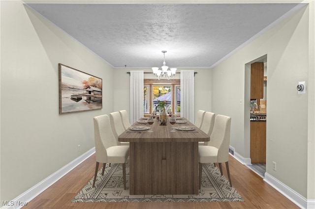 dining room featuring crown molding, a textured ceiling, an inviting chandelier, and hardwood / wood-style floors