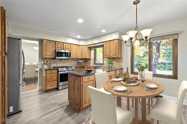 kitchen with hanging light fixtures, backsplash, a kitchen island, light wood-type flooring, and stainless steel appliances