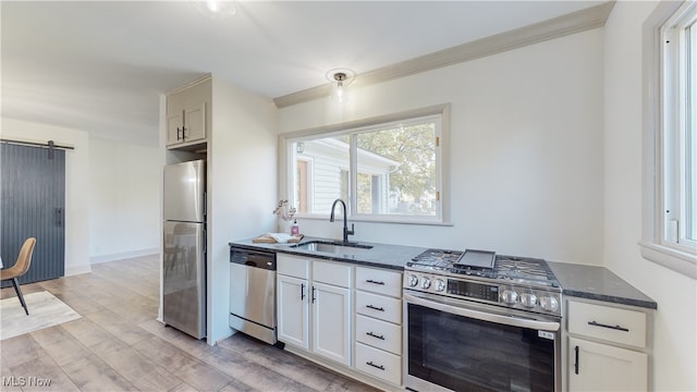 kitchen featuring white cabinetry, a barn door, sink, light hardwood / wood-style floors, and stainless steel appliances