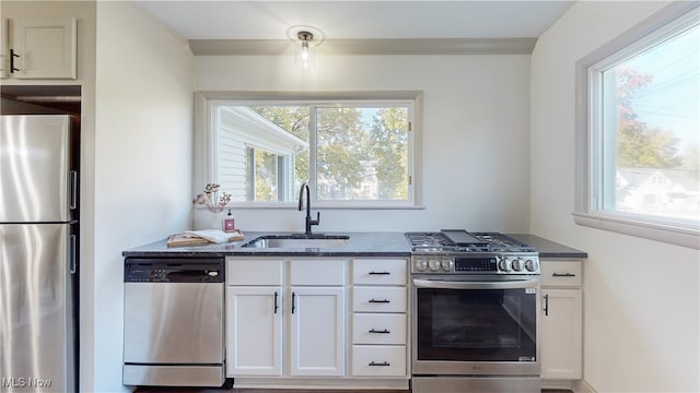 kitchen featuring sink, white cabinetry, stainless steel appliances, dark stone countertops, and crown molding