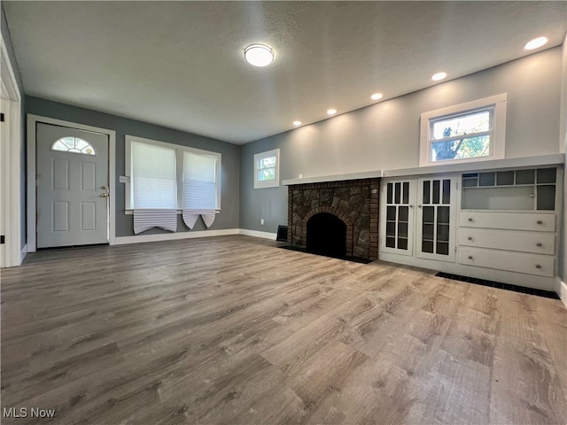 unfurnished living room featuring hardwood / wood-style floors, a brick fireplace, and a textured ceiling