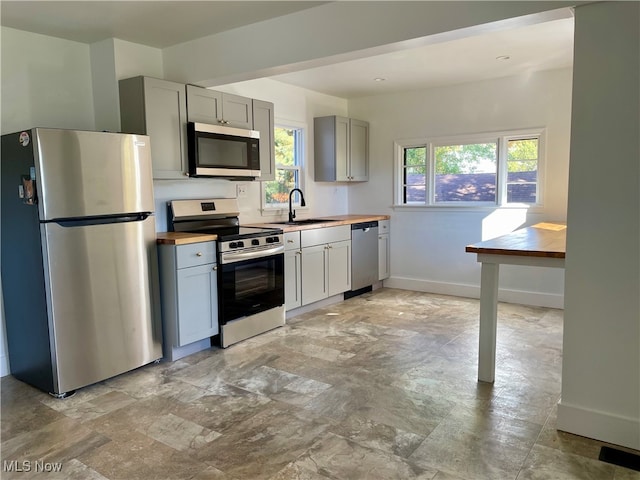 kitchen featuring a healthy amount of sunlight, stainless steel appliances, wood counters, and gray cabinets