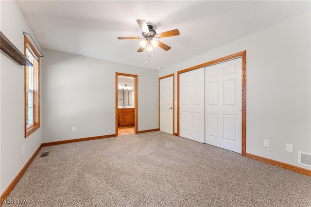 unfurnished bedroom with a closet, ensuite bathroom, light colored carpet, and ceiling fan