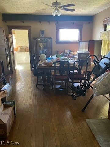 dining room featuring hardwood / wood-style flooring, ceiling fan, a fireplace, and a textured ceiling