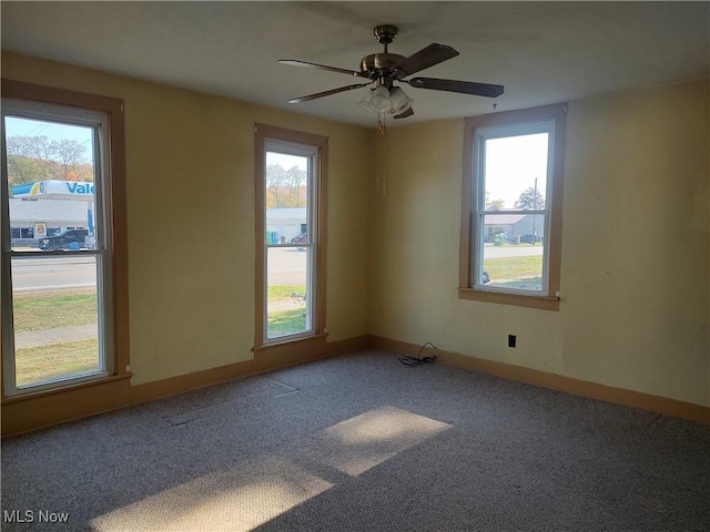 carpeted spare room featuring ceiling fan and baseboards