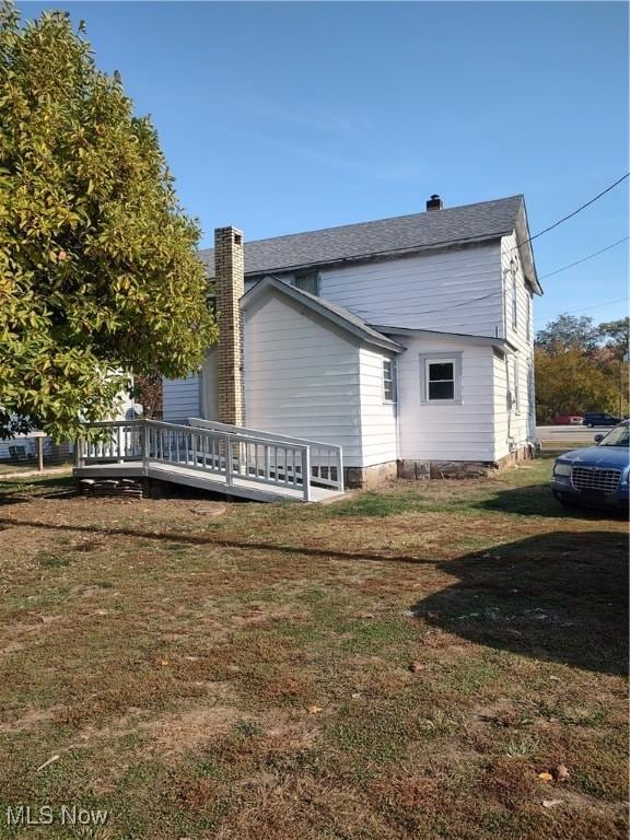 view of side of property featuring a chimney, a deck, and a yard