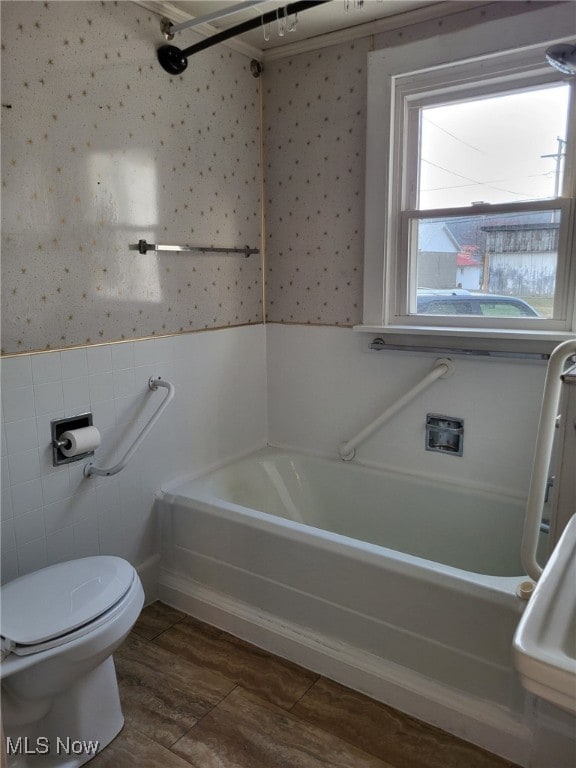 bathroom featuring a tub to relax in, wallpapered walls, toilet, a wainscoted wall, and tile walls