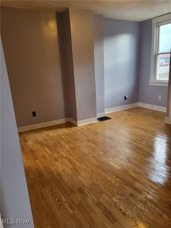 unfurnished room with a textured ceiling, baseboards, and wood finished floors