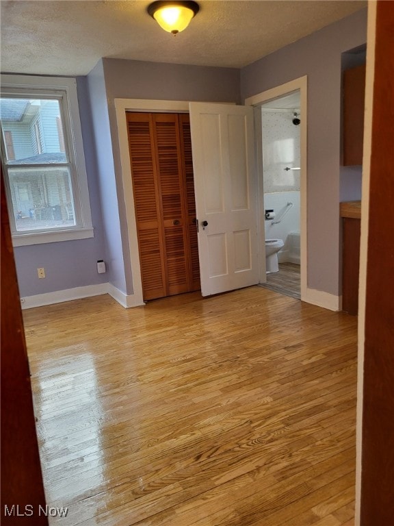 unfurnished bedroom featuring light wood-style flooring, a textured ceiling, baseboards, and a closet