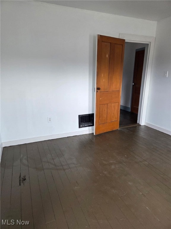 spare room featuring dark wood-style flooring, visible vents, and baseboards