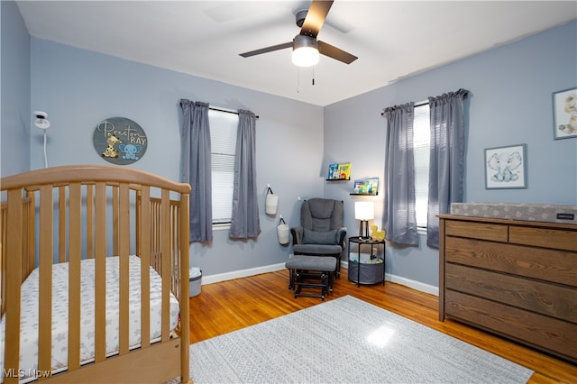 bedroom with a crib, wood-type flooring, and ceiling fan