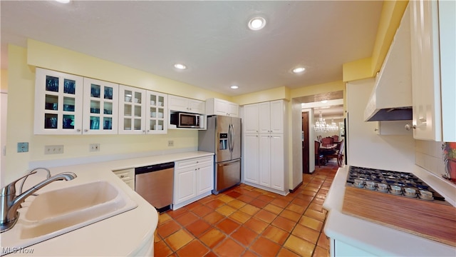 kitchen with custom range hood, stainless steel appliances, sink, a chandelier, and white cabinetry