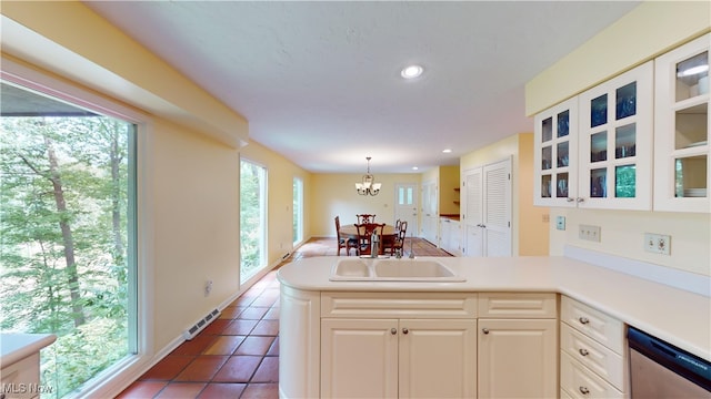 kitchen featuring dark tile patterned flooring, sink, dishwasher, kitchen peninsula, and an inviting chandelier