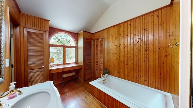 bathroom featuring lofted ceiling, a tub, hardwood / wood-style floors, and wood walls