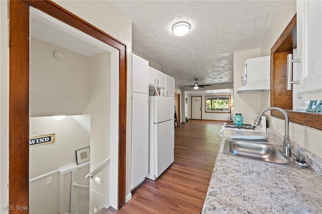 kitchen with white fridge, dark wood-type flooring, sink, and white cabinets