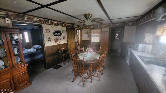 dining space featuring wood walls, sink, carpet, and ceiling fan