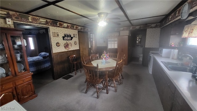 carpeted dining space with ceiling fan, wood walls, and sink